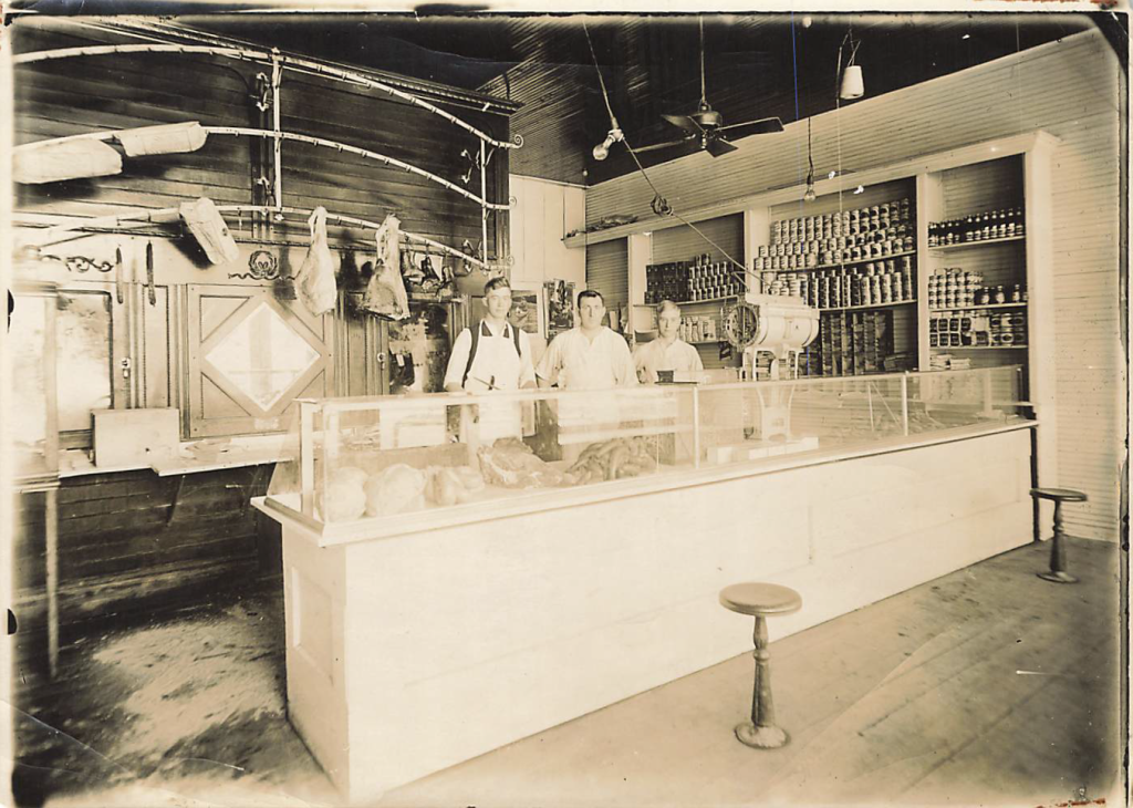 3 men standing behind a meat counter in a black and white photo